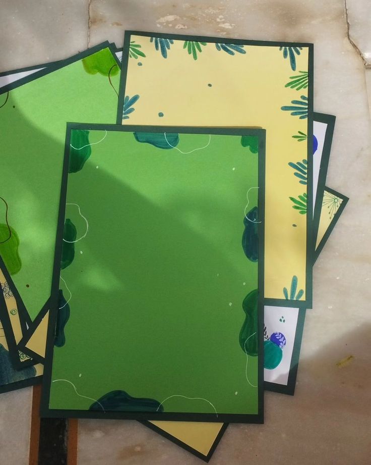 four pieces of green and yellow paper sitting on top of each other in front of a mirror