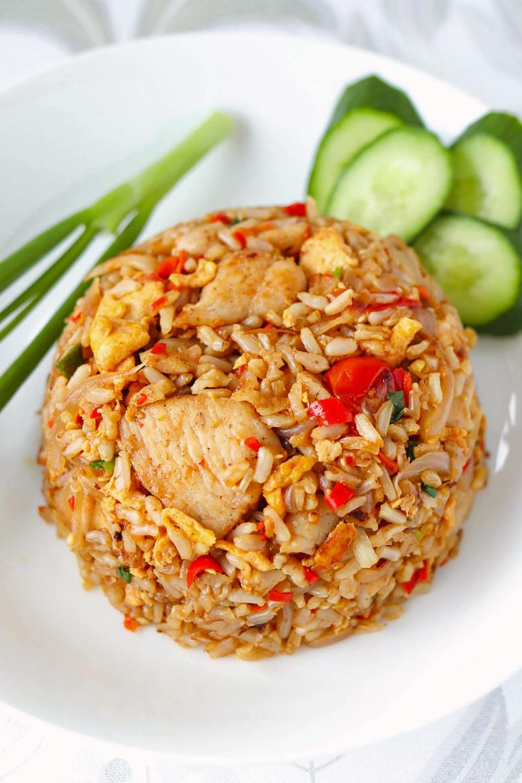 a white plate topped with fried rice and veggies next to cucumbers