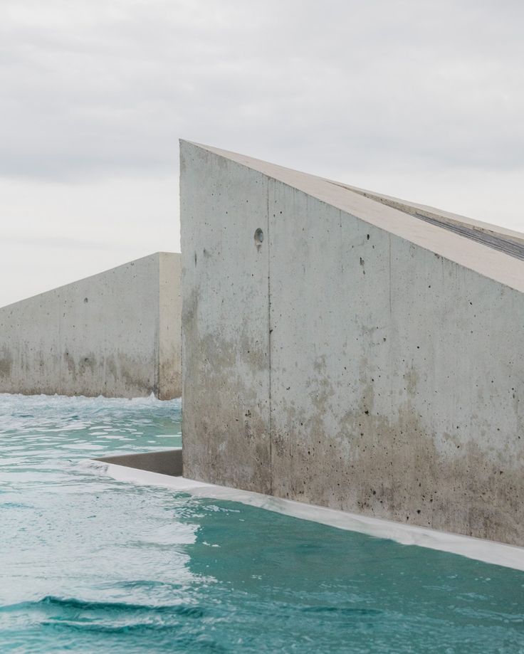 a concrete wall next to the ocean under a cloudy sky