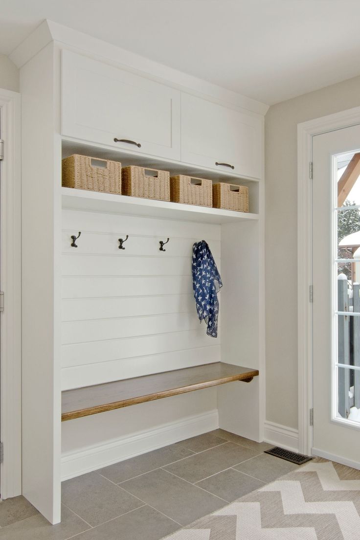 a white bench sitting under a window next to a coat rack