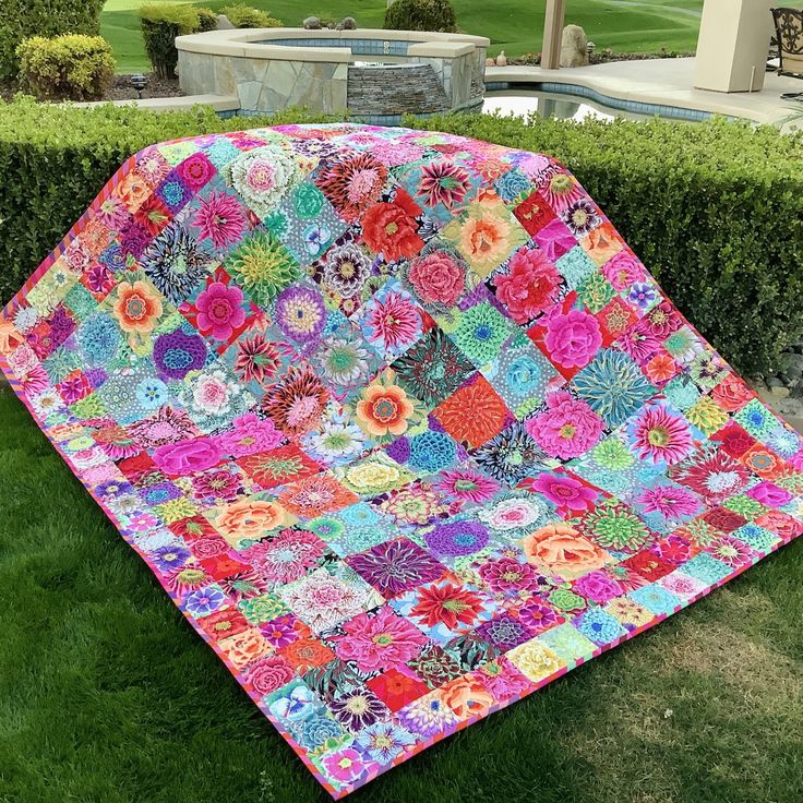 a colorful quilt sitting on top of a lush green field