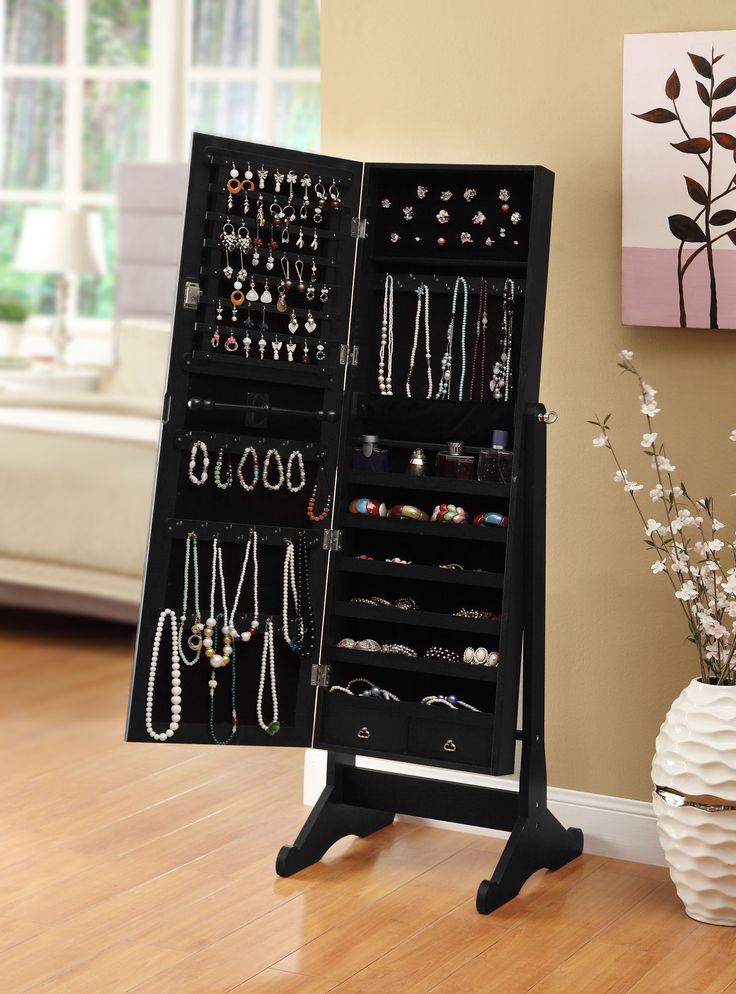 a black jewelry cabinet sitting on top of a wooden floor next to a vase filled with flowers