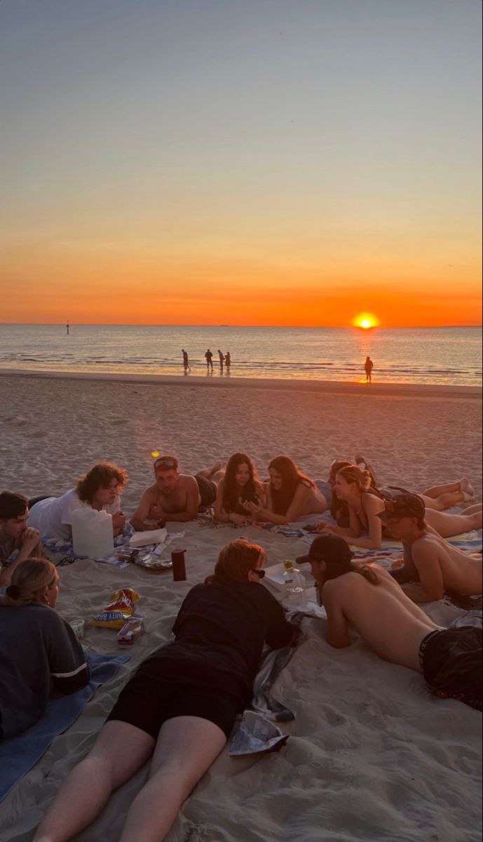 a group of people laying on top of a beach next to the ocean at sunset