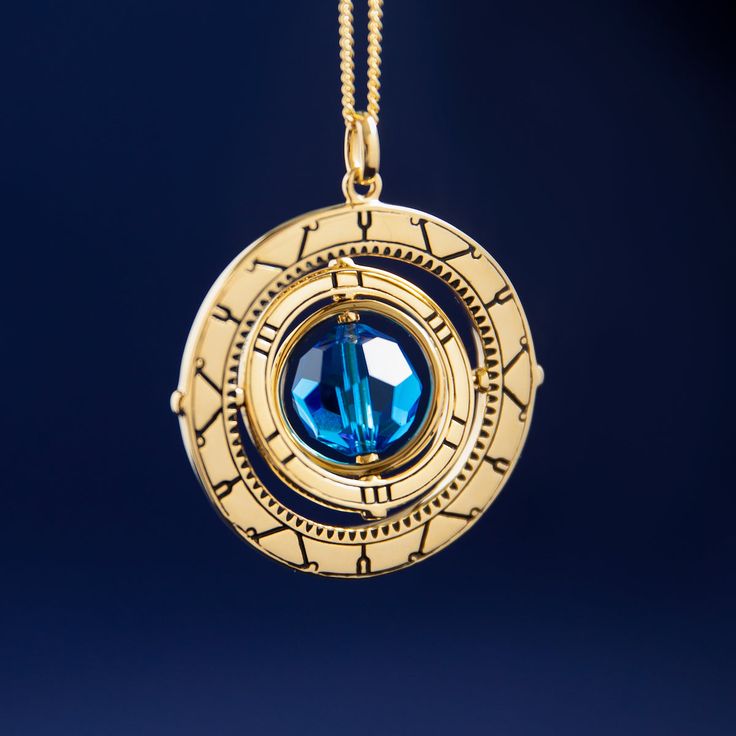 a gold necklace with a blue stone in the center on a chain against a dark background