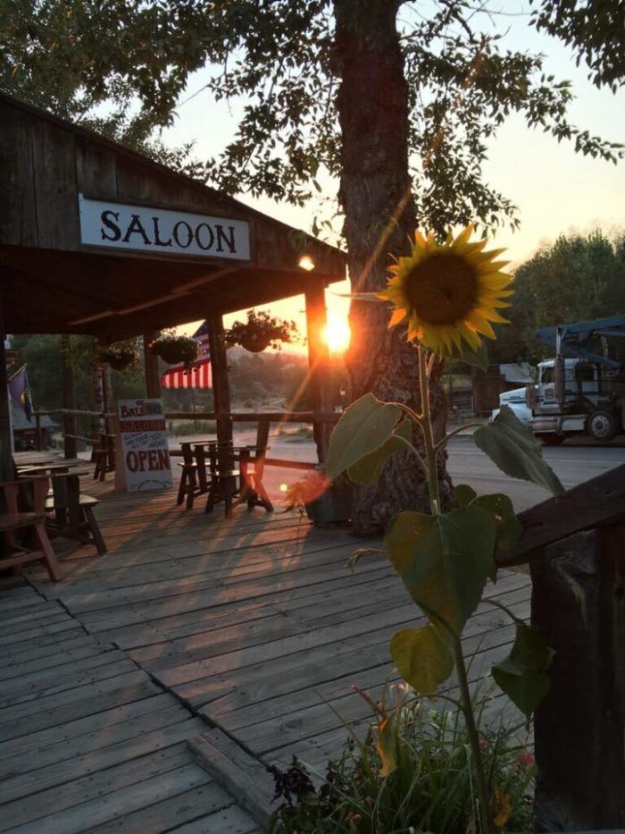 the sun is setting at saloon with tables and benches in front of it, along with a large sunflower