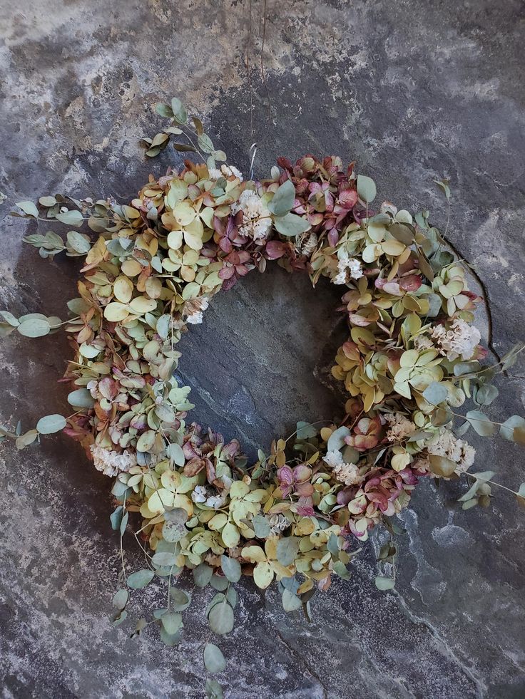 a wreath made out of leaves and flowers on a stone surface with the word love written in it