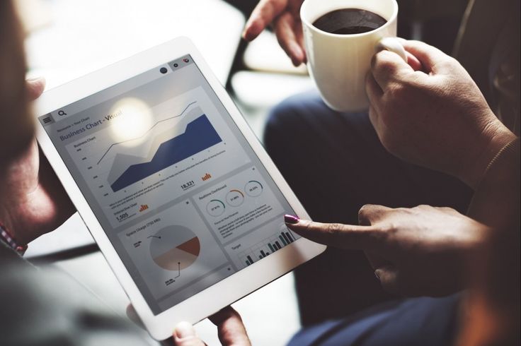 two people are looking at a tablet with graphs on it and coffee in front of them