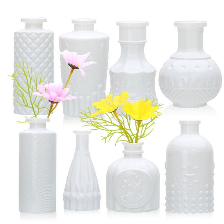 several white vases with yellow and pink flowers in each one, on a white background