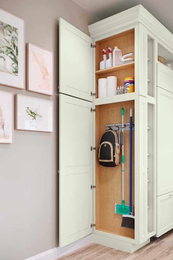 a white cabinet filled with lots of cleaning supplies next to a wall mounted toilet paper dispenser