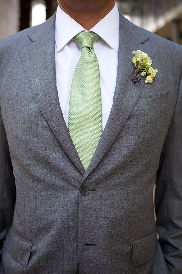 a man wearing a gray suit with a green tie and flower boutonniere