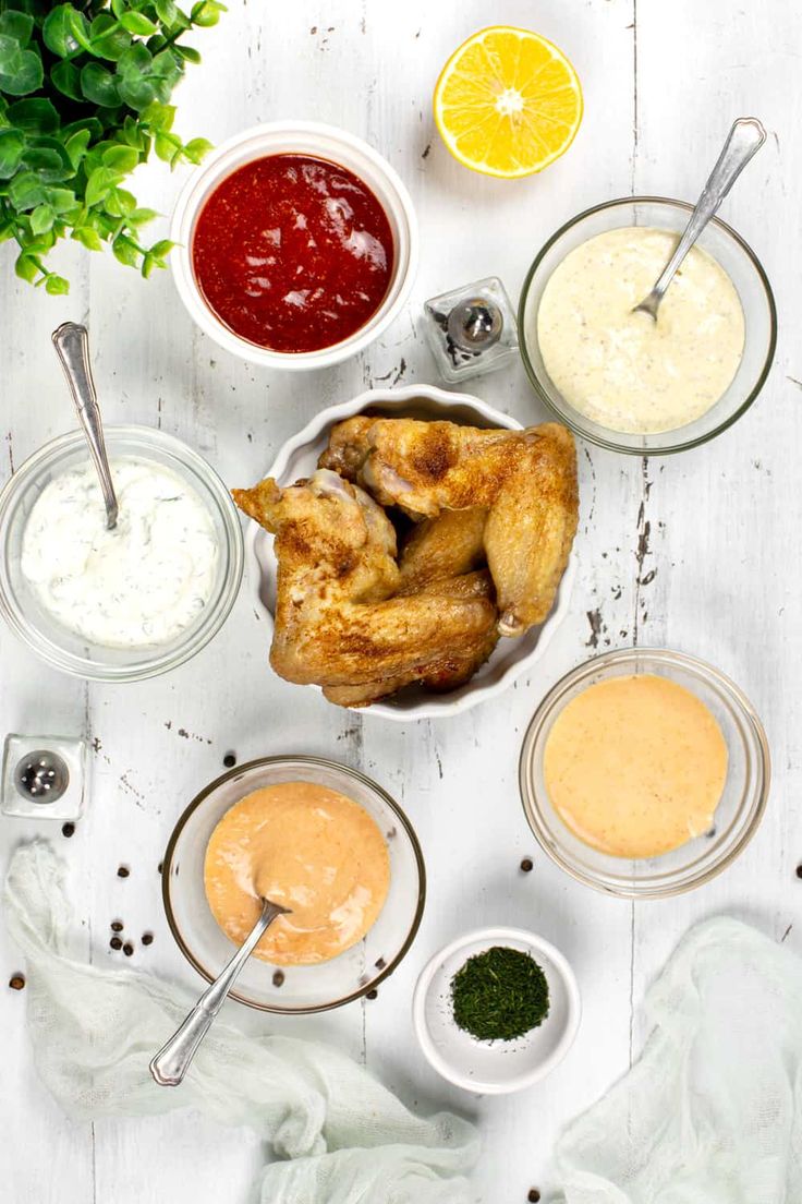 an overhead shot of chicken wings, sauces and lemon wedges on a white table