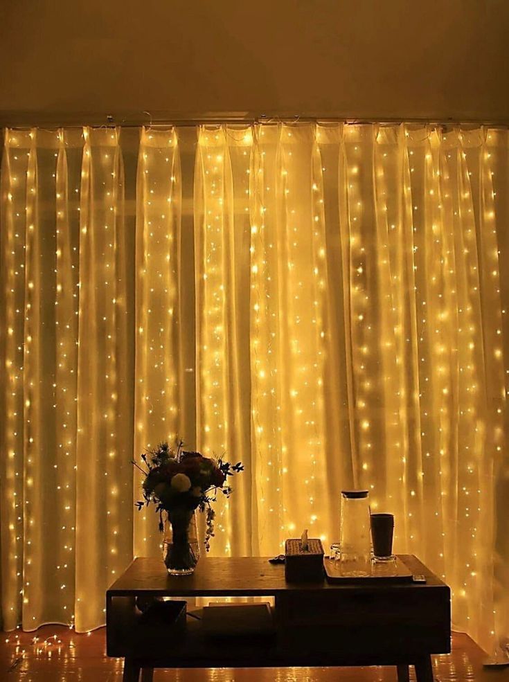 a living room with lights on the curtains and a vase filled with flowers in front of it