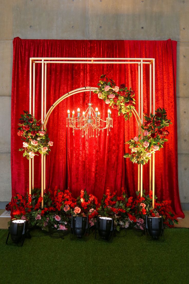 a red backdrop with chandelier and flowers on it, along with potted plants