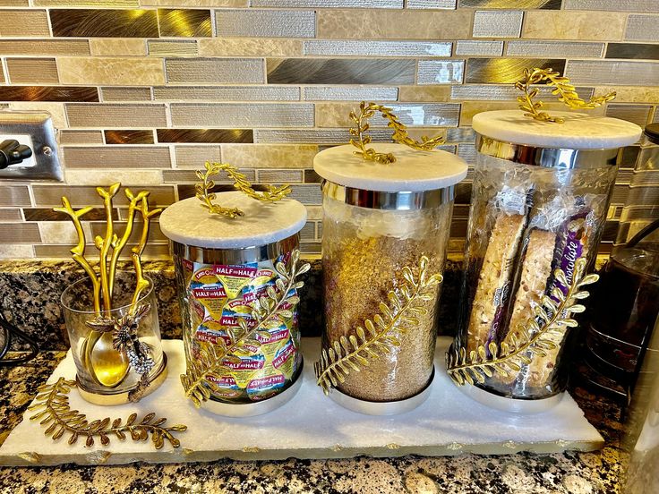 three jars filled with different types of items on a counter top next to a tile backsplash