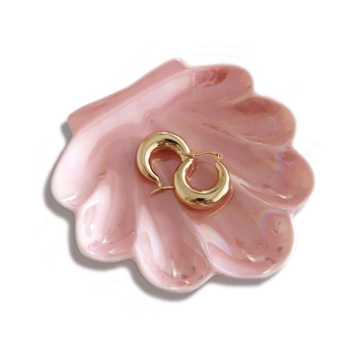 a pair of gold hoop earrings sitting on top of a pink flower shaped brooch