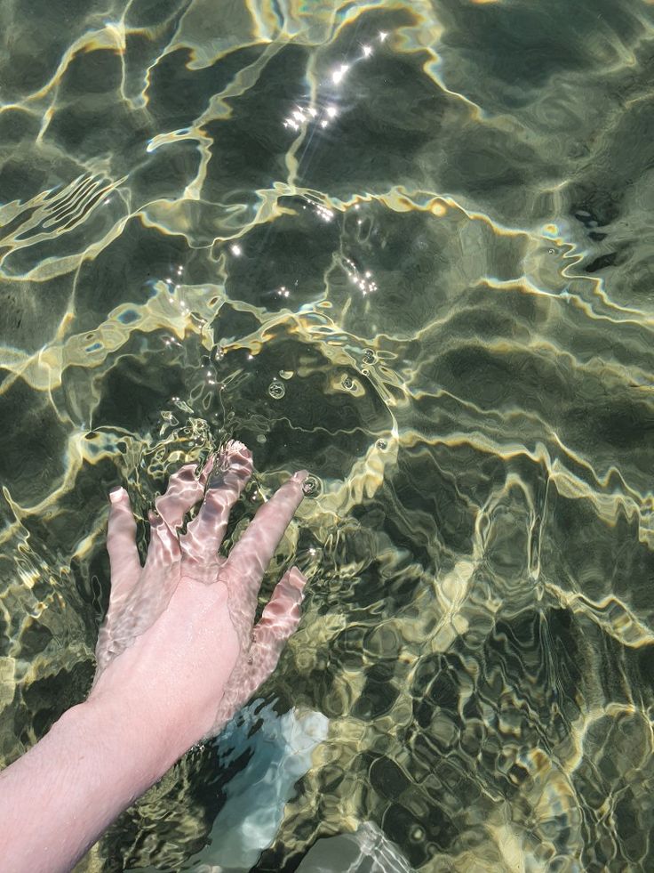 a person's hand reaching for something in the clear blue water that they are swimming in