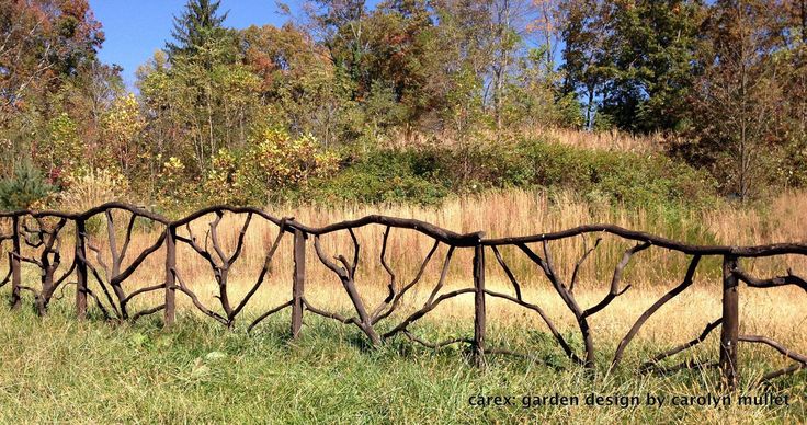 a wooden fence made out of branches in the middle of a field with grass and trees behind it