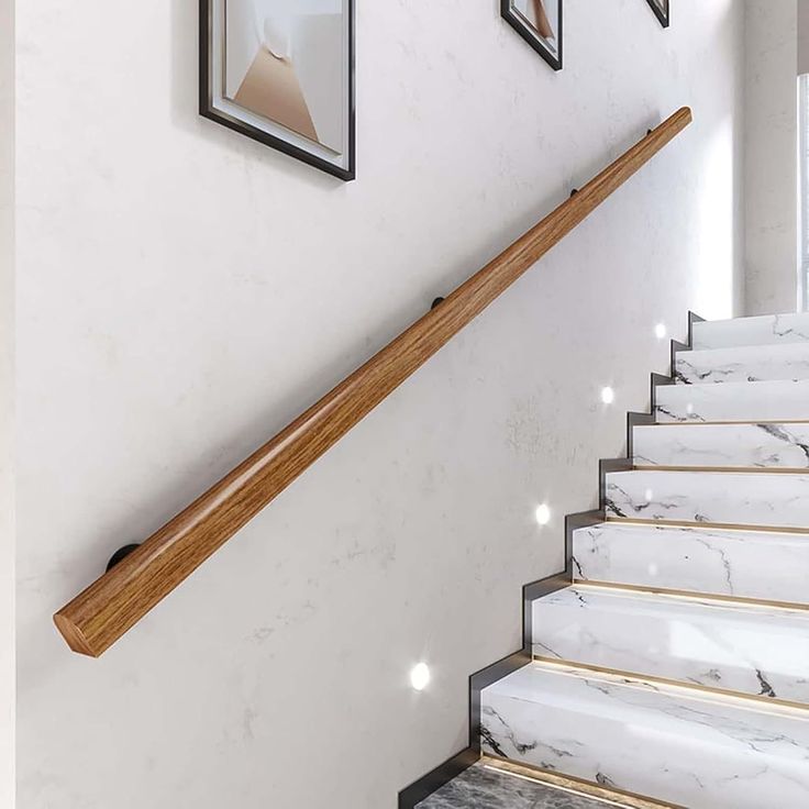 there are pictures on the wall next to the stairs in this house with marble steps and wood handrails