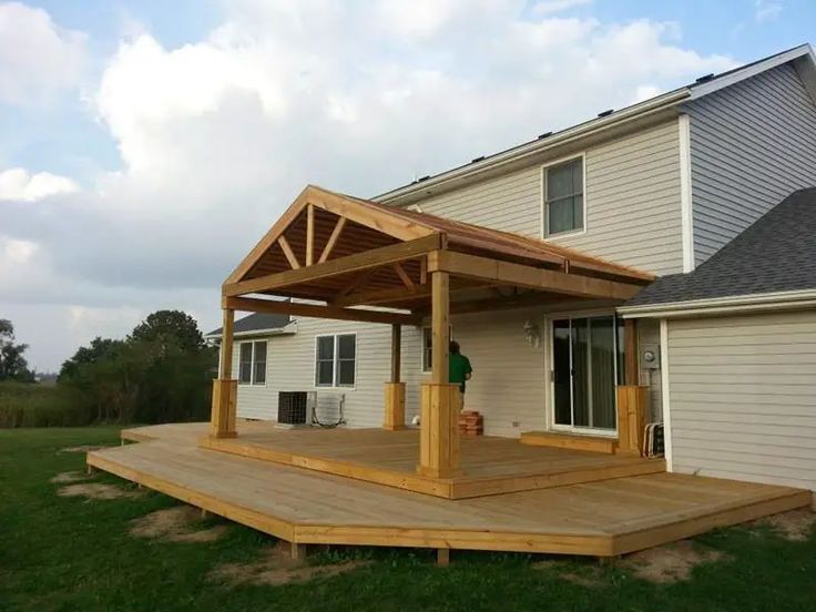 a wooden deck in front of a house with a covered patio and attached hot tub