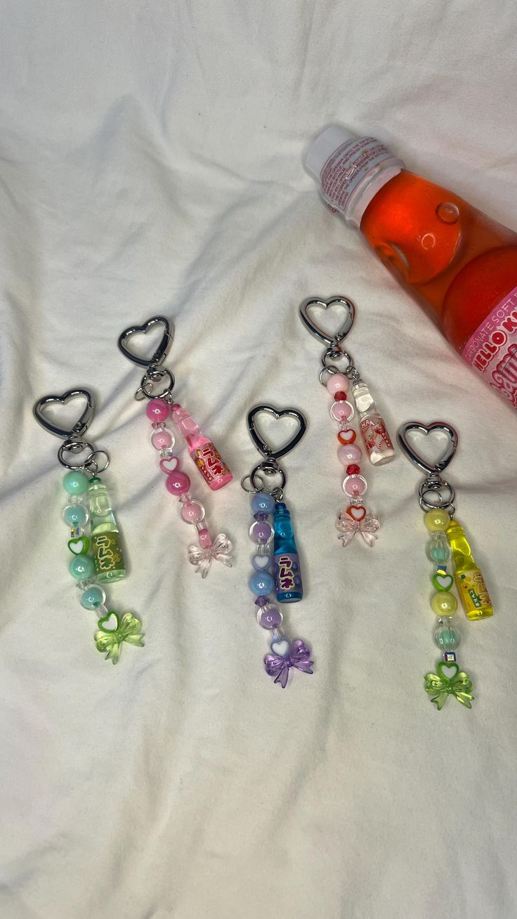 four keychains with hearts and beads hanging from them on a white sheet next to an orange bottle