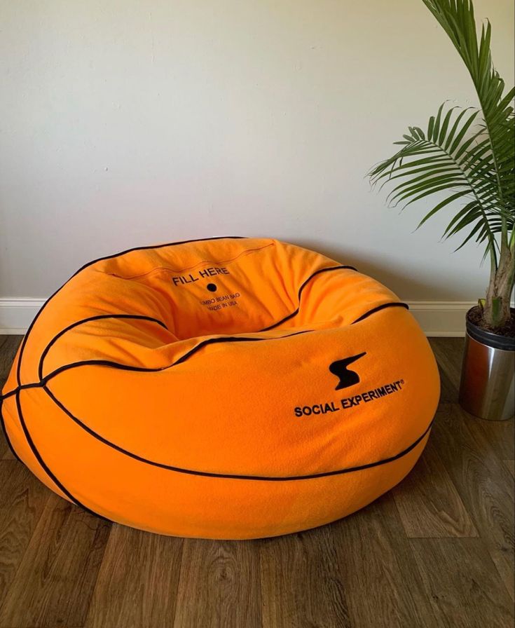 an orange bean bag chair sitting on top of a wooden floor next to a potted plant