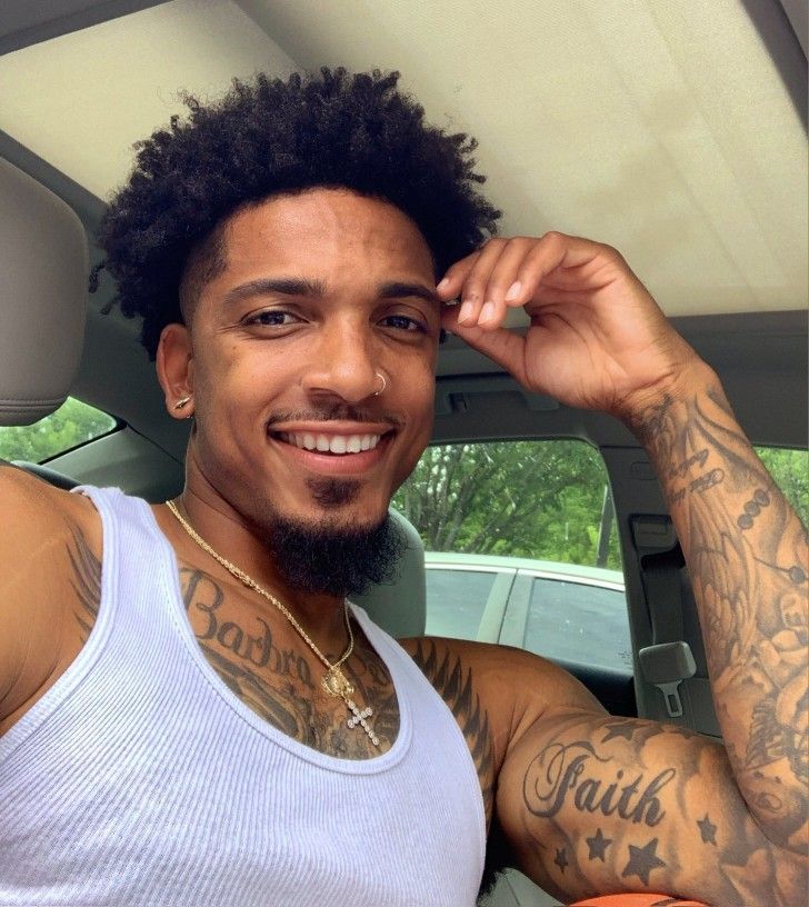 a man with tattoos on his arms and chest sitting in a car smiling at the camera