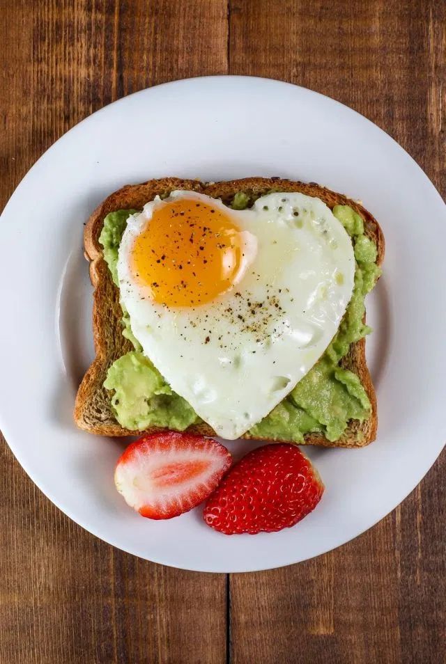 an egg in the shape of a heart on toast with strawberries and avocado