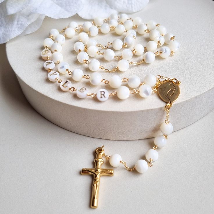 This Personalized Rosary, is ideal as a Baptism gift for a little girl or baby boy or as a gift for a special occasion. It is expertly handcrafted in a traditional style with a contemporary twist utilizing genuine Mother of pearl stone and gold-plated brass wire, which not only gives a touch of nature but also tenderness. The letter beads on the Rosary are also handmade from genuine mother of pearl, and the length is perfect to worn as a dainty Rosary necklace for women. MATCHING ROSARY BRACELET White Spiritual Jewelry For Gifts, Gift Rosary With 8mm Round Beads, Rosary With 8mm Round Beads As Gift, 8mm Round Bead Rosary As Gift, White Spiritual Cross Jewelry And Charms, Pearl White Rosary With 8mm Beads As Gift, Adjustable Round Rosary As Gift, Mother's Day Gift Rosary With 8mm Beads, Adjustable White Rosary For First Communion