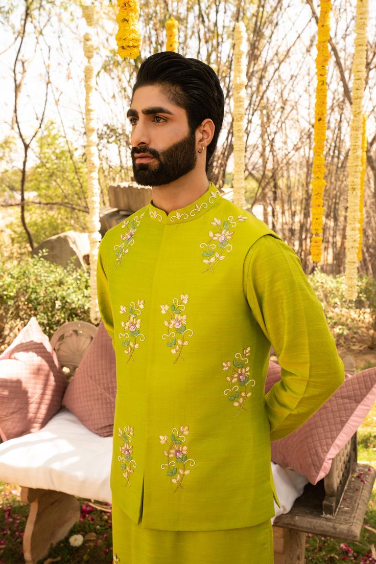 a man wearing a green outfit standing in front of a bed with flowers on it