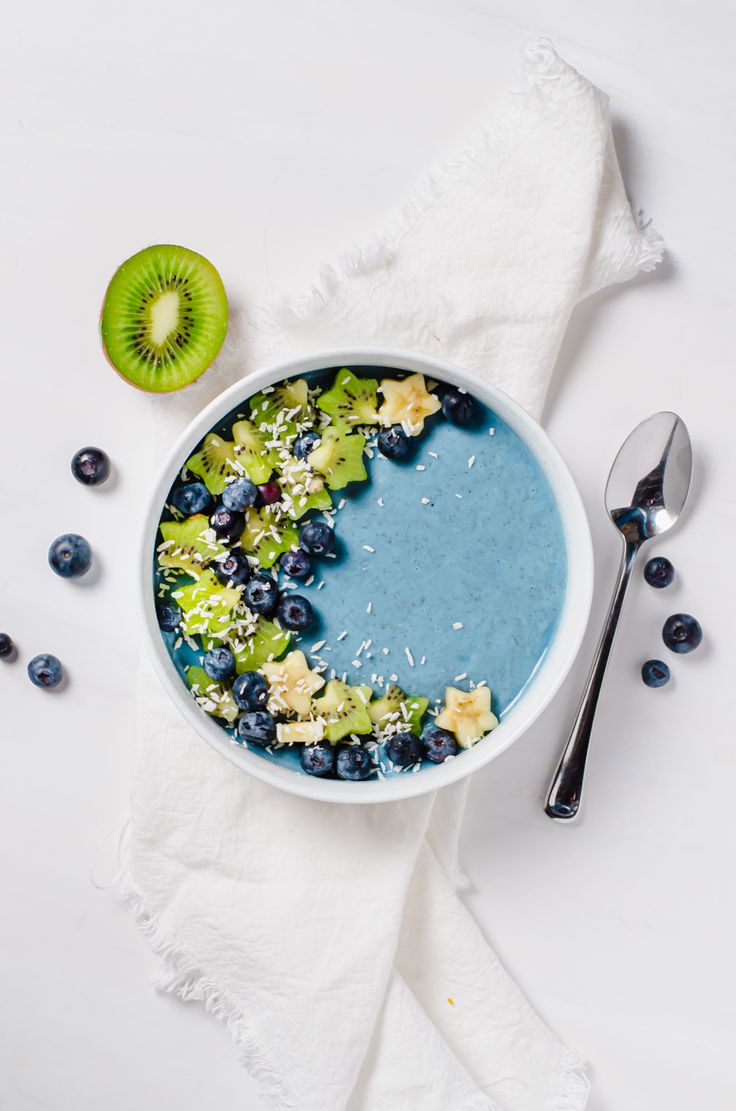 a bowl filled with blueberries, kiwis and other fruits next to a spoon