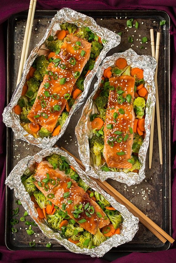 three trays filled with salmon and vegetables on top of purple cloth next to chopsticks