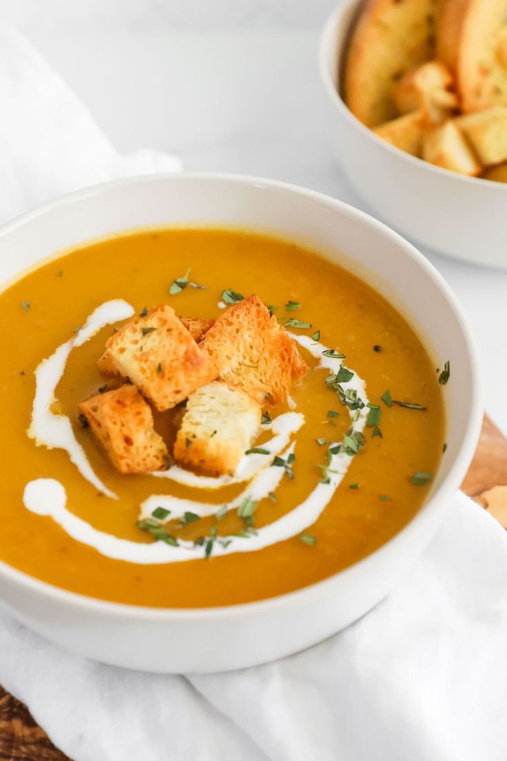 two bowls filled with soup and croutons on top of a white cloth napkin