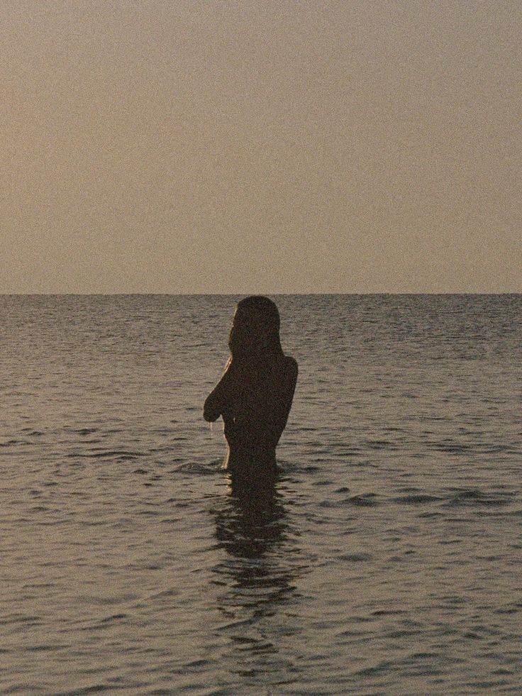 a woman standing in the ocean at sunset