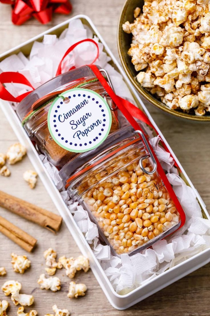 two glass jars filled with popcorn next to a bowl of cinnamon sugar popcorn on a table