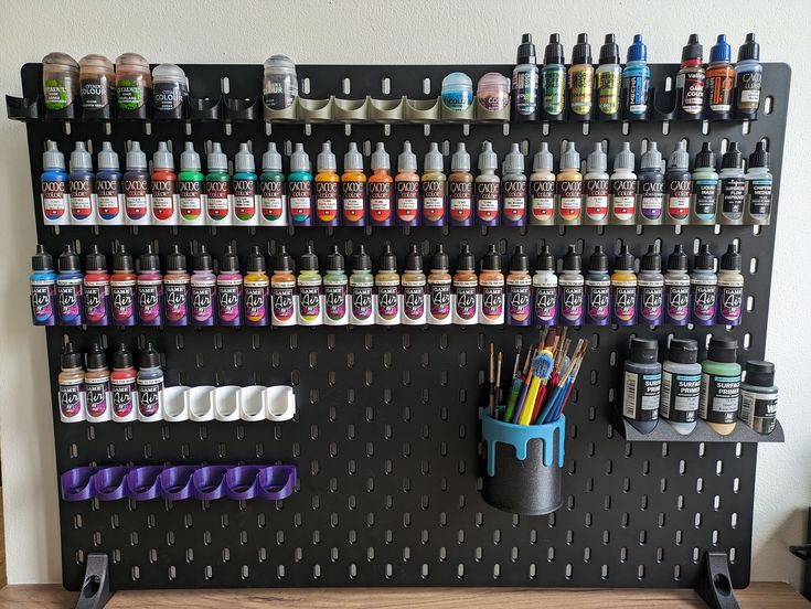 a peg board with lots of paint bottles on it and a cup full of pens