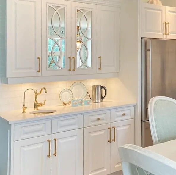 a kitchen with white cabinets and marble counter tops, gold pulls on the door handles