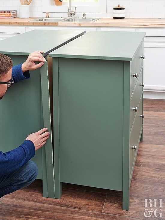 a man is working on a green cabinet in the middle of a kitchen with wood floors