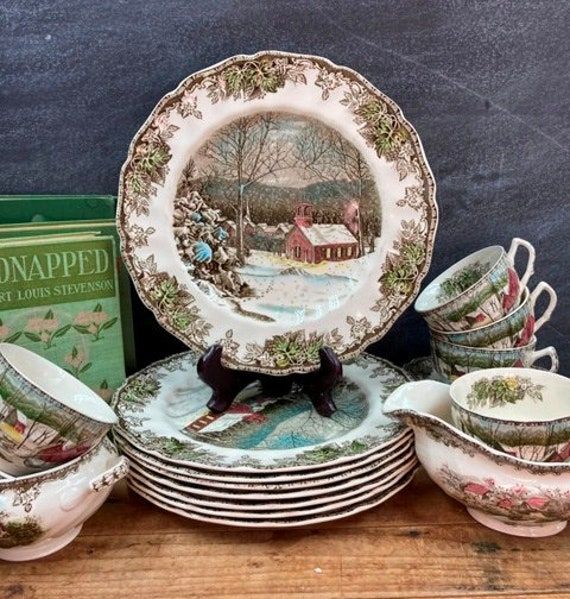 a table topped with lots of plates and bowls next to a boxed book on top of a wooden table