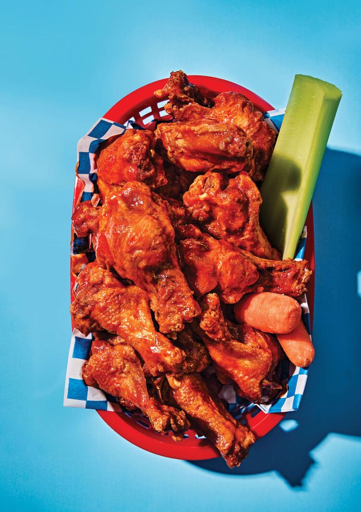 chicken wings and celery in a red bowl on a blue tablecloth with a spoon