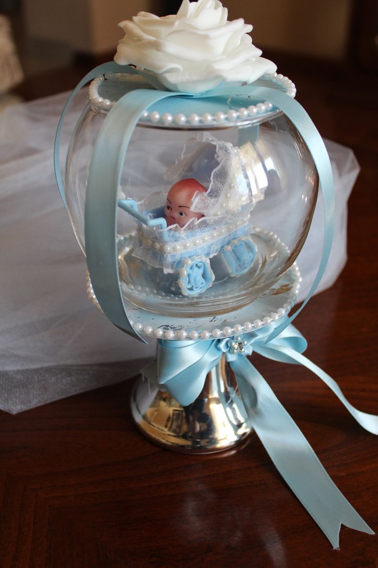 a baby doll in a carriage under a glass dome with blue ribbon around the base