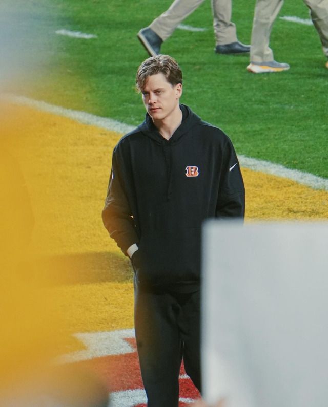 a man standing on top of a baseball field wearing a black jacket and pants with his hands in his pockets