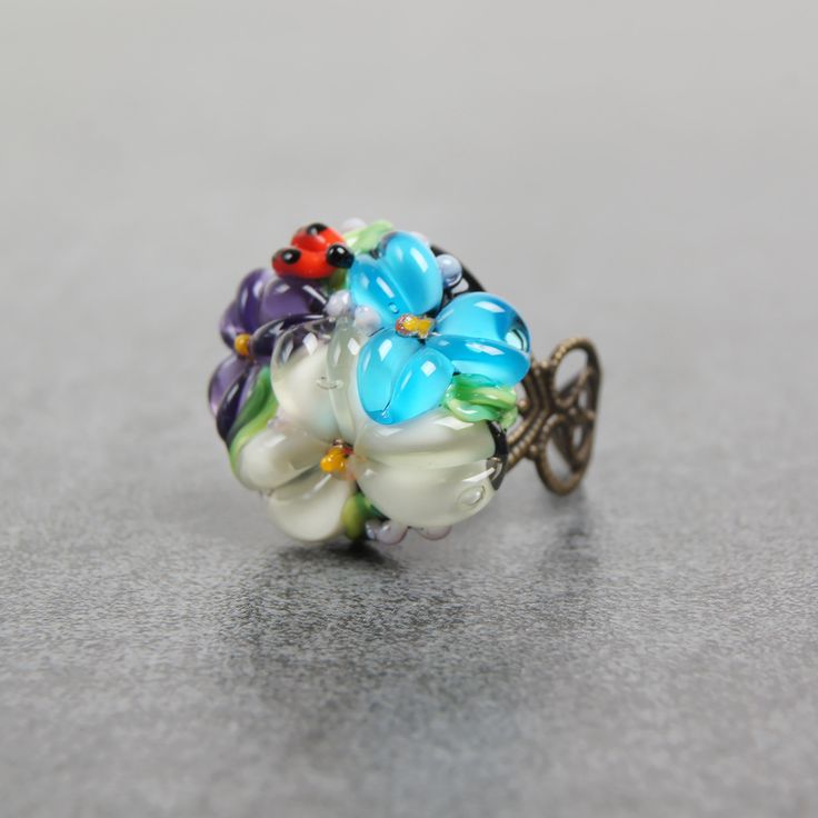 This romantic Glass ladybug flower ring is a perfect gift for women. It's very tender and unique! Set Matching bracelet: https://www.etsy.com/listing/161559547 Matching earrings: https://www.etsy.com/listing/200833152 Matching pendant: https://www.etsy.com/listing/161556072 Dimensions: the ring is adjustable. The bead is 2.2-2.4cm in diameter. Materials: artist lampwork bead, metal fittings. Colors used: blue, white, lilac, violet, green. Please, note, each bead is made by hand and may differ sl Dainty Jewelry With Handmade Flowers For Gift, Dainty Jewelry With Handmade Flowers As Gift, Whimsical Adjustable Ring, Whimsical Adjustable Jewelry Ring, Adjustable Whimsical Ring, Delicate Flower Ring As Gift, Whimsical Flower Shaped Jewelry For Gift, Whimsical Flower Shaped Jewelry As Gift, Whimsical Flower Shaped Jewelry Gift