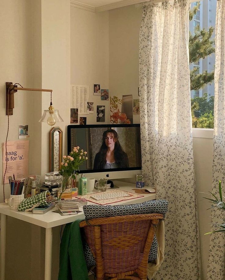 a desk with a computer on top of it in front of a window covered by curtains