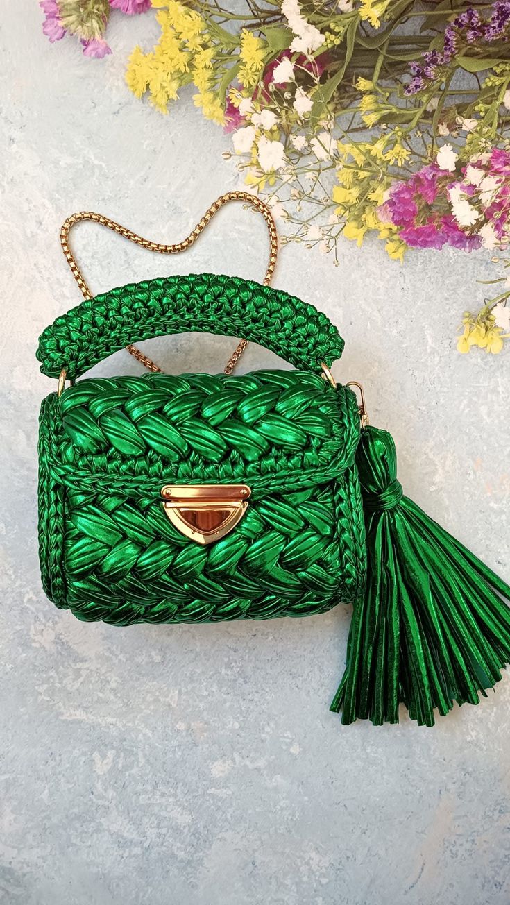 a green handbag sitting on top of a white table next to some purple flowers