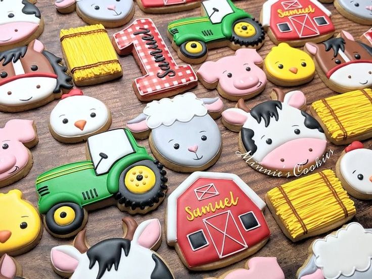 decorated cookies with farm animals and tractors are displayed on a wooden table in front of the camera