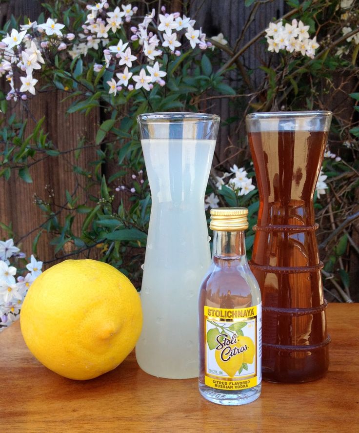 three different types of alcohol sitting on a table next to flowers and a vase with lemons