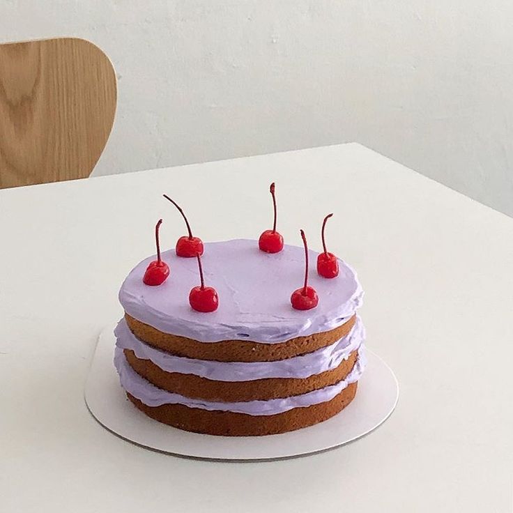 a cake with white frosting and cherries on top is sitting on a table