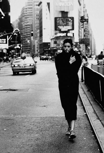 a black and white photo of a woman walking down the street with her hand on her chest