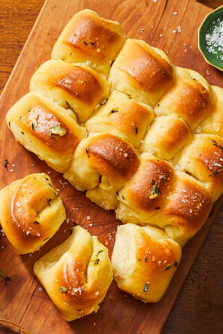 a wooden cutting board topped with rolls covered in cheese and seasoning next to a bowl of salt