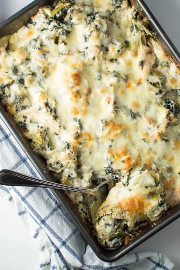 a casserole dish with cheese and spinach on top, next to a spoon